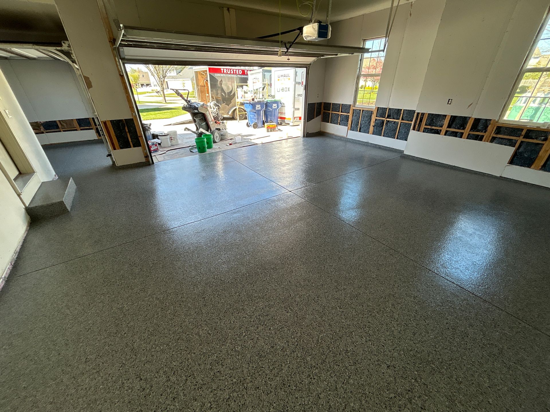 Empty indoor space with polished speckled floor, large windows, and a view of a green cart outside