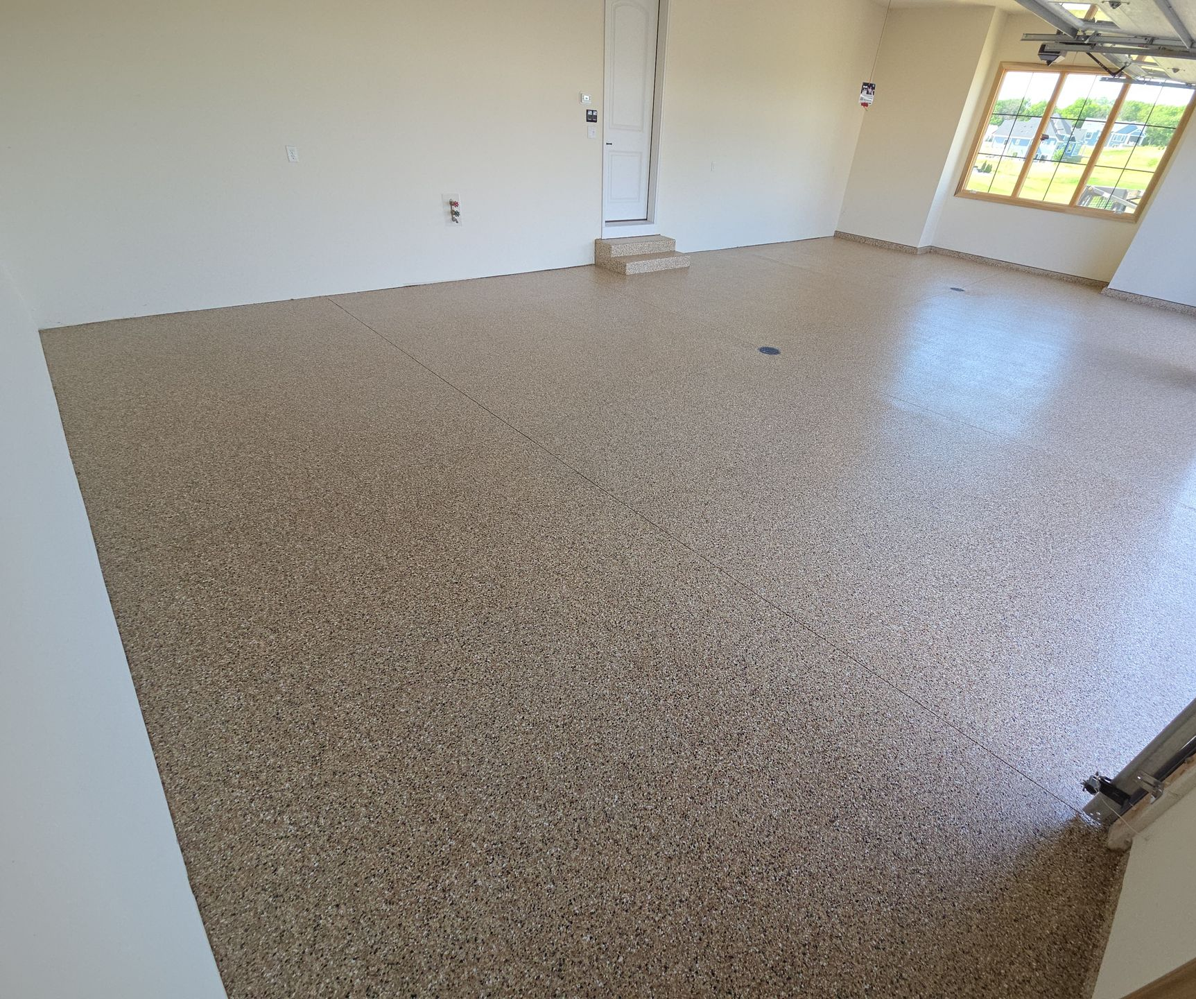 Empty room with speckled floor, white walls, and a window letting in daylight
