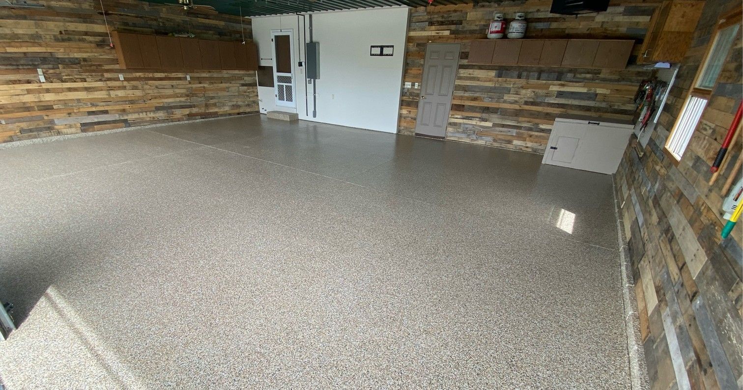Empty rustic room with wood-plank walls and a speckled gray floor, viewed from the corner.