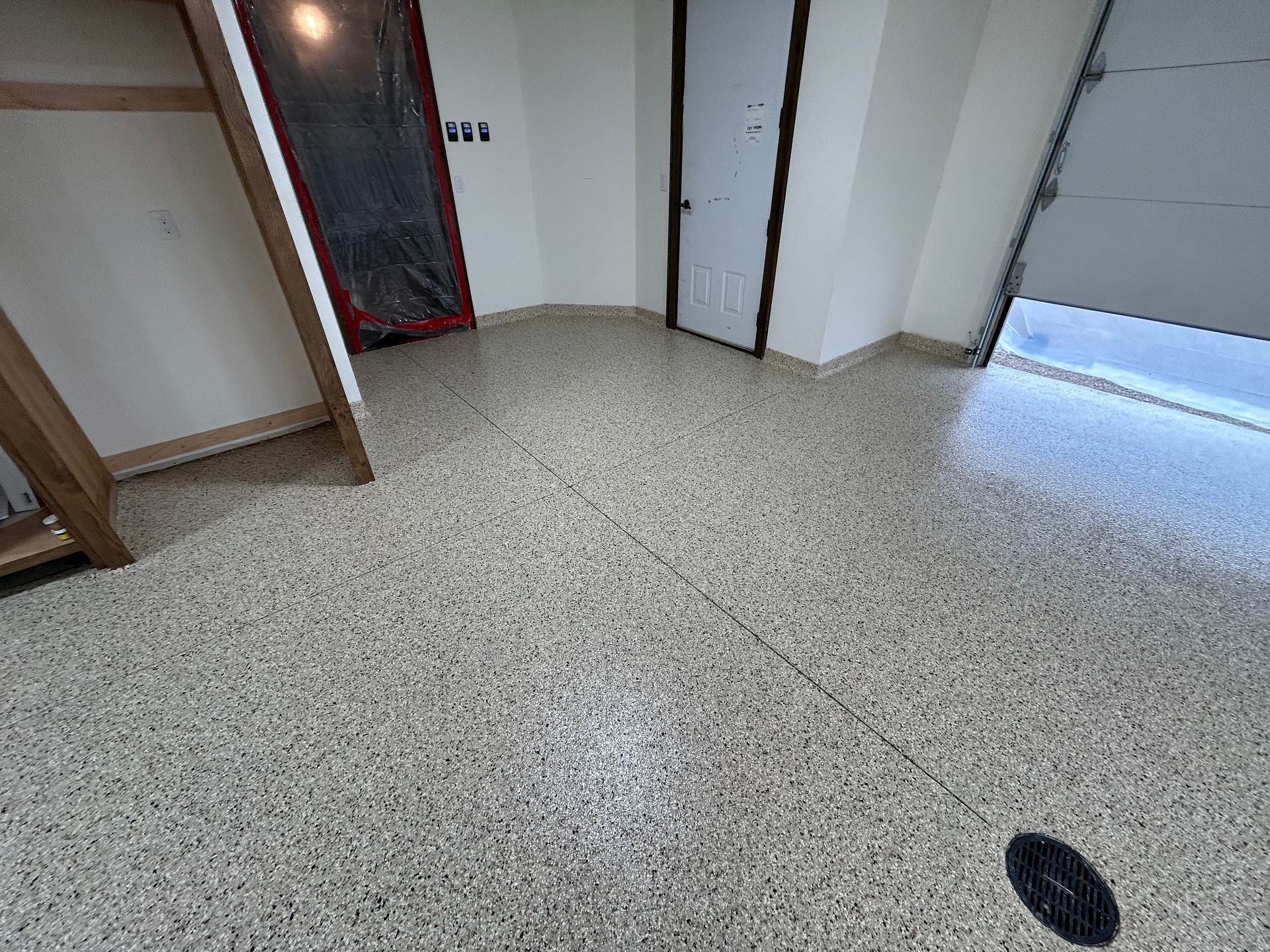 Empty indoor room with speckled floor, white walls, open doorway, and a floor drain