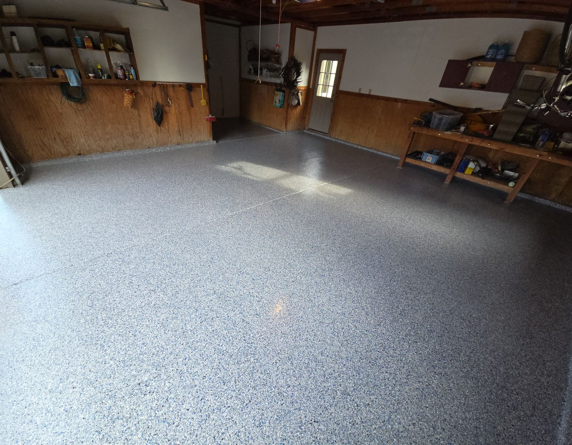 Empty garage with speckled epoxy floor, wood-paneled walls, and shelves along the back and right sides