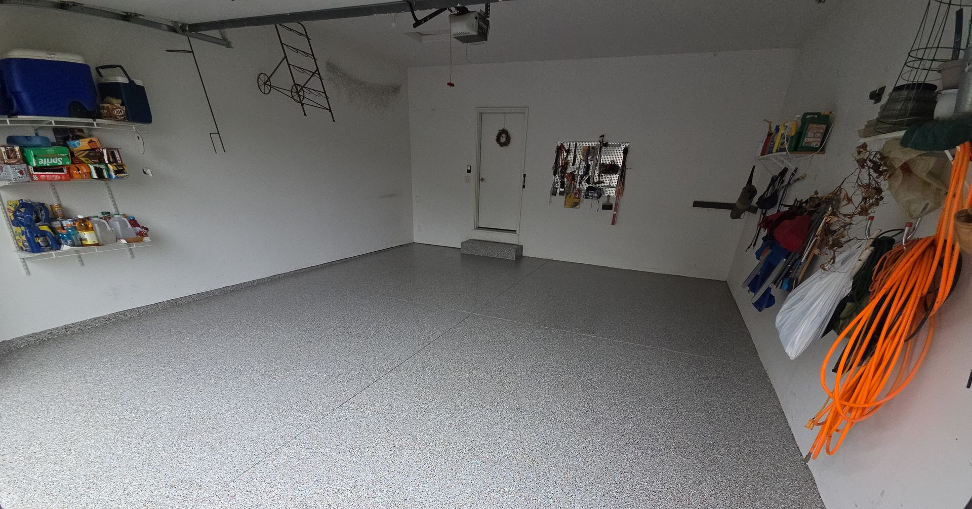 Empty garage with gray speckled floor, white walls, and stored tools along the sides