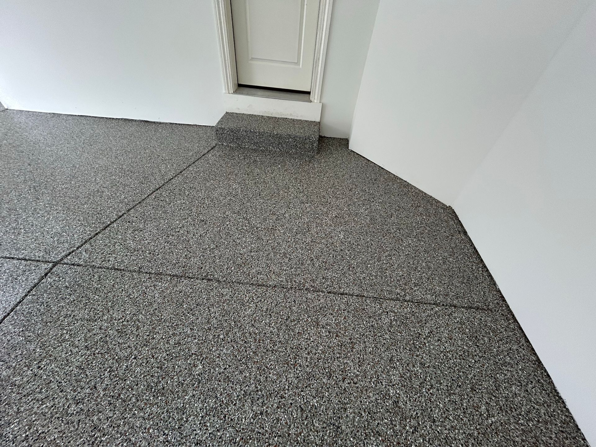 Speckled gray carpeted floor meeting white walls in a hallway corner with a narrow doorway opening