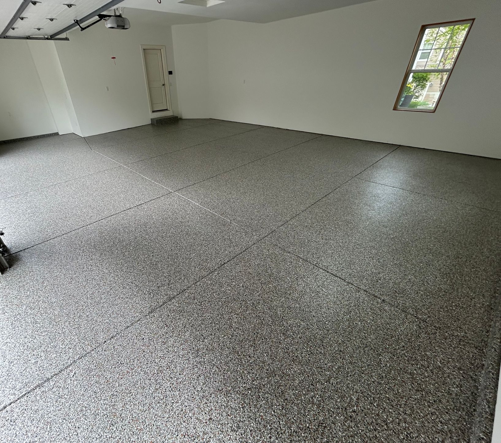 Empty garage with gray speckled floor, white walls, and a small window.