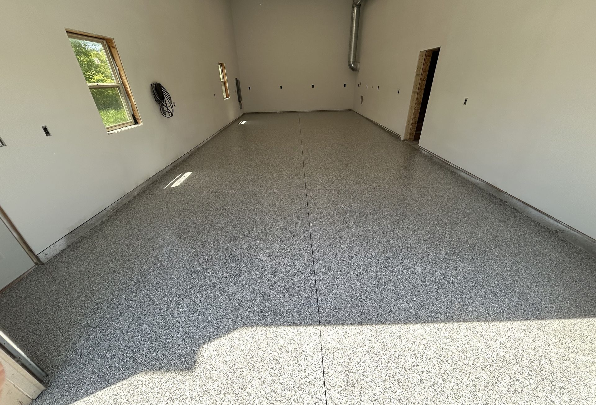 Empty garage interior with speckled concrete floor, white walls, and open doorways