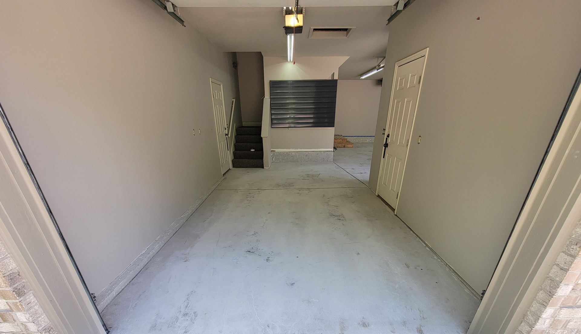 Empty garage with white walls, concrete floor, and a back staircase leading to a closed door.