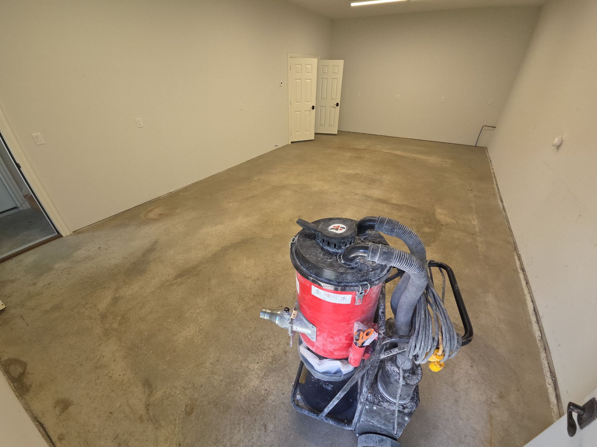 Empty room with stained concrete floor and a red vacuum or floor buffer in the foreground