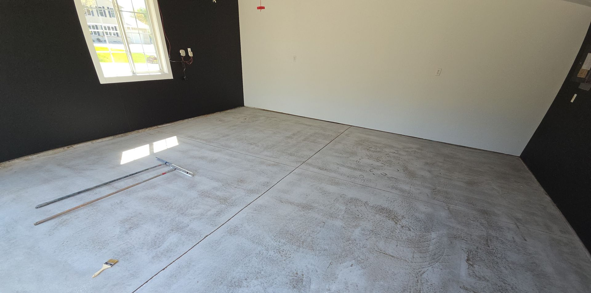 Empty concrete room with bare floor, white walls, and a window letting in sunlight.