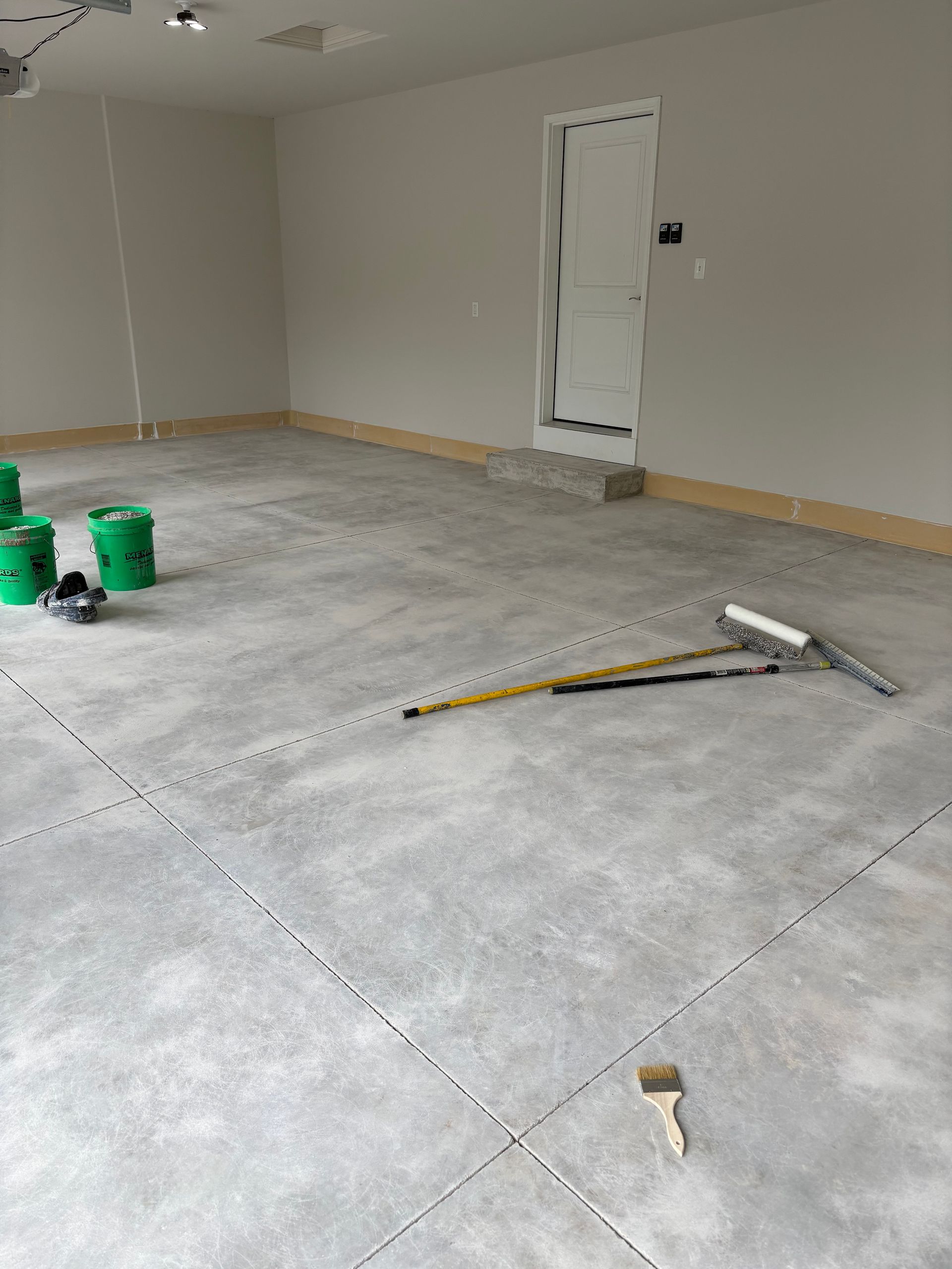Empty room with unfinished concrete floor, tools scattered, and a door on the far wall.
