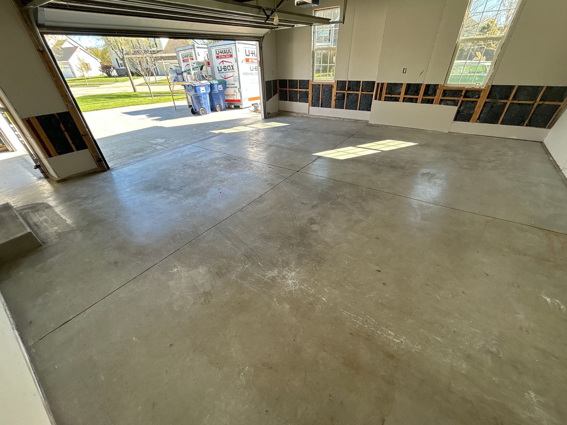 Empty garage with concrete floor and open door to a sunny driveway.