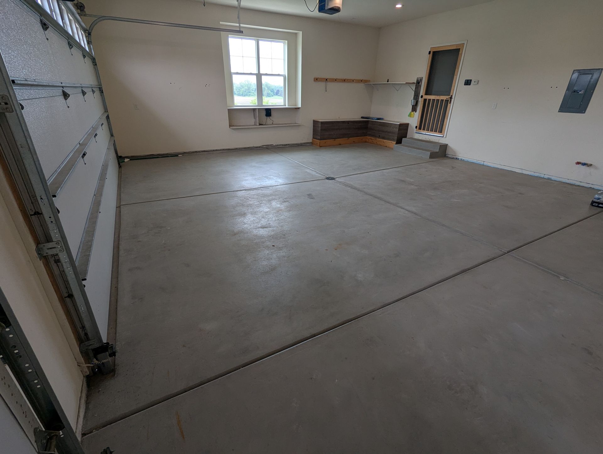Empty garage interior with concrete floor, open garage door, and a small window on the back wall