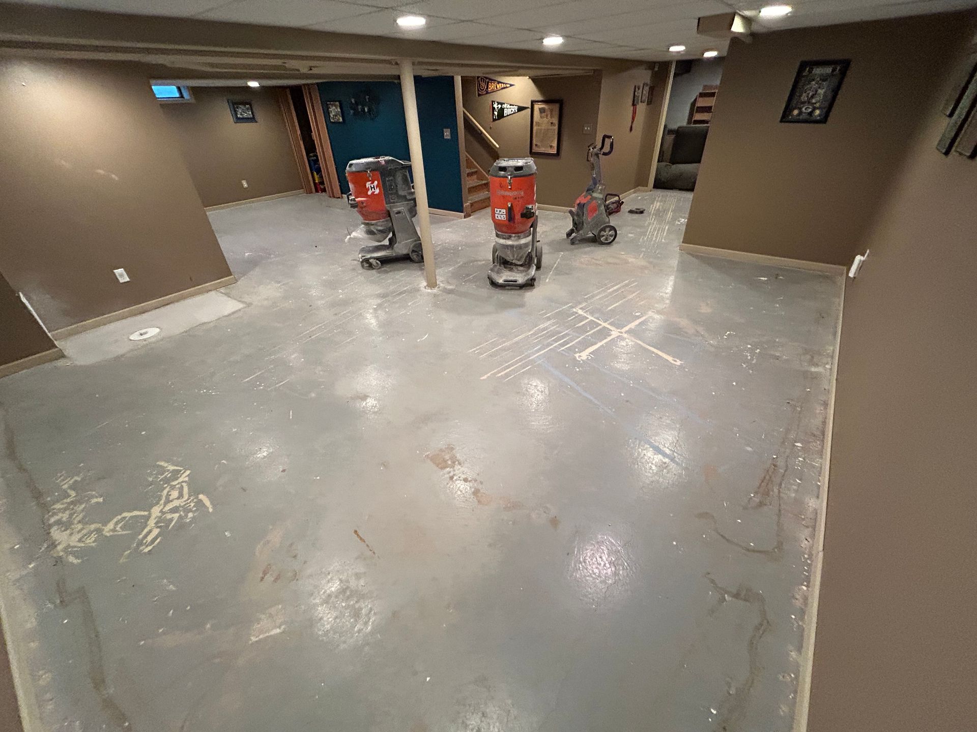 Empty basement room with polished concrete floor, brown walls, and a red cart near the center.