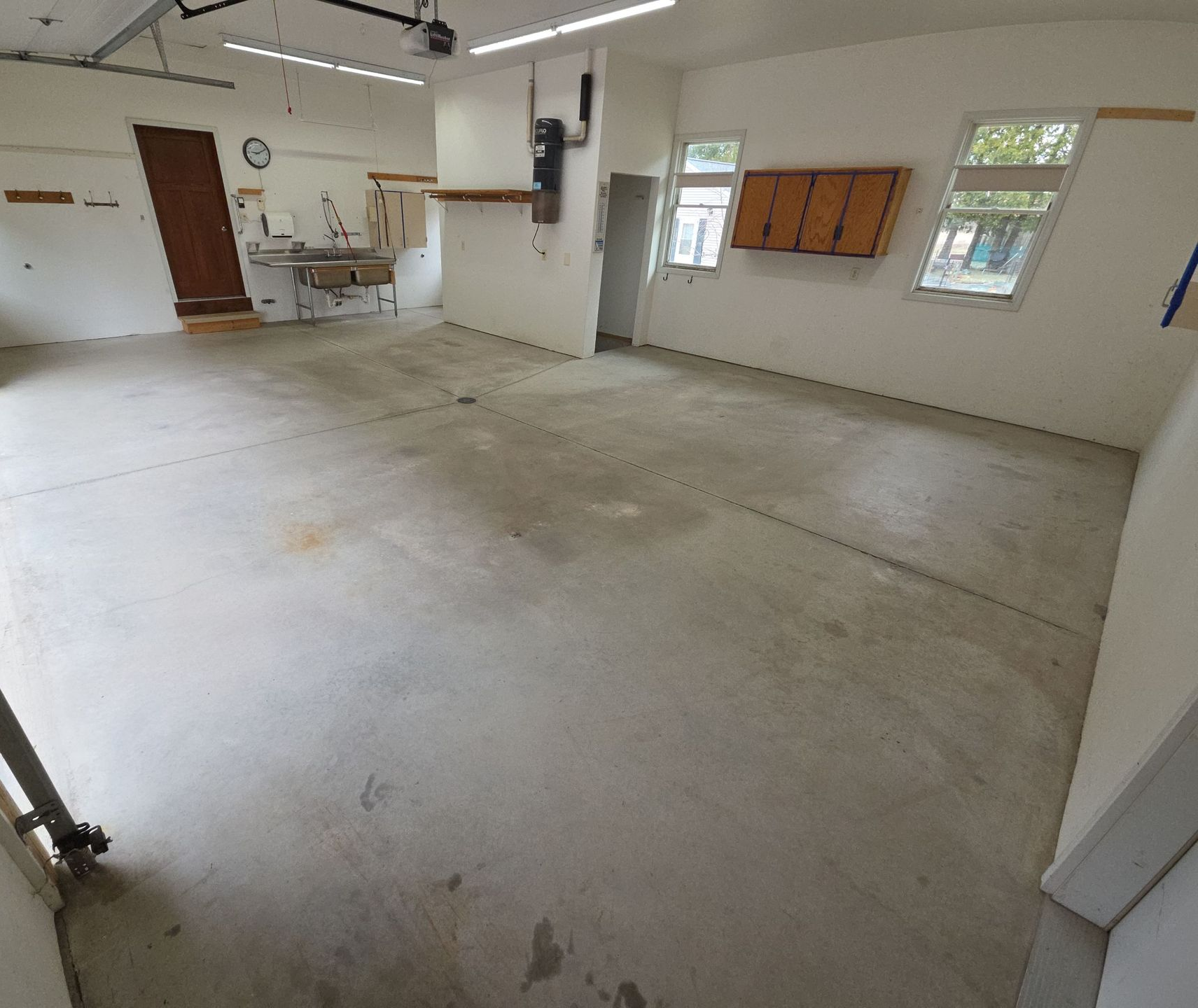 Empty garage or workshop with a concrete floor, white walls, and windows letting in daylight