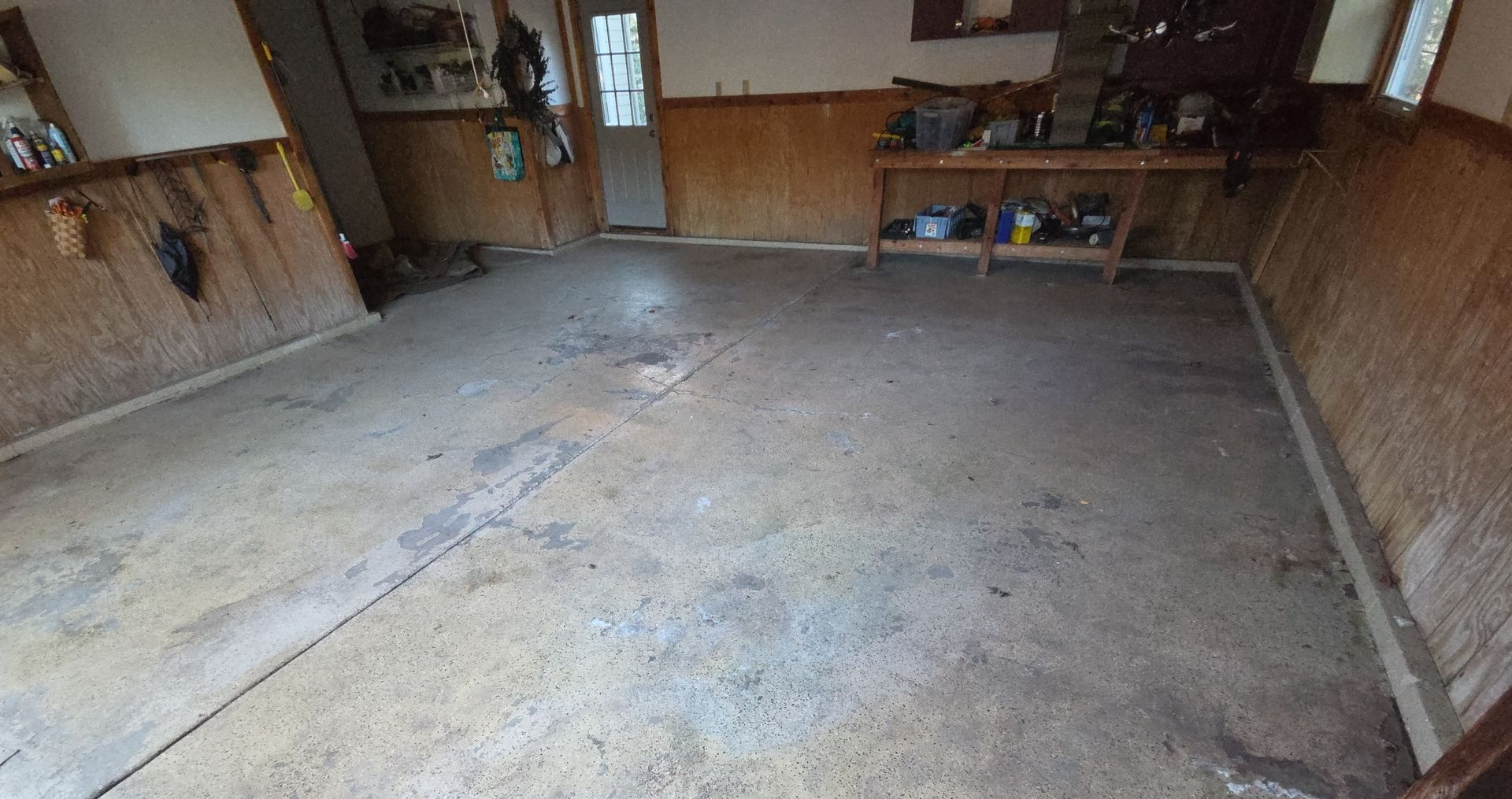 Empty concrete garage with bare walls, shelves, and a workbench in the back.