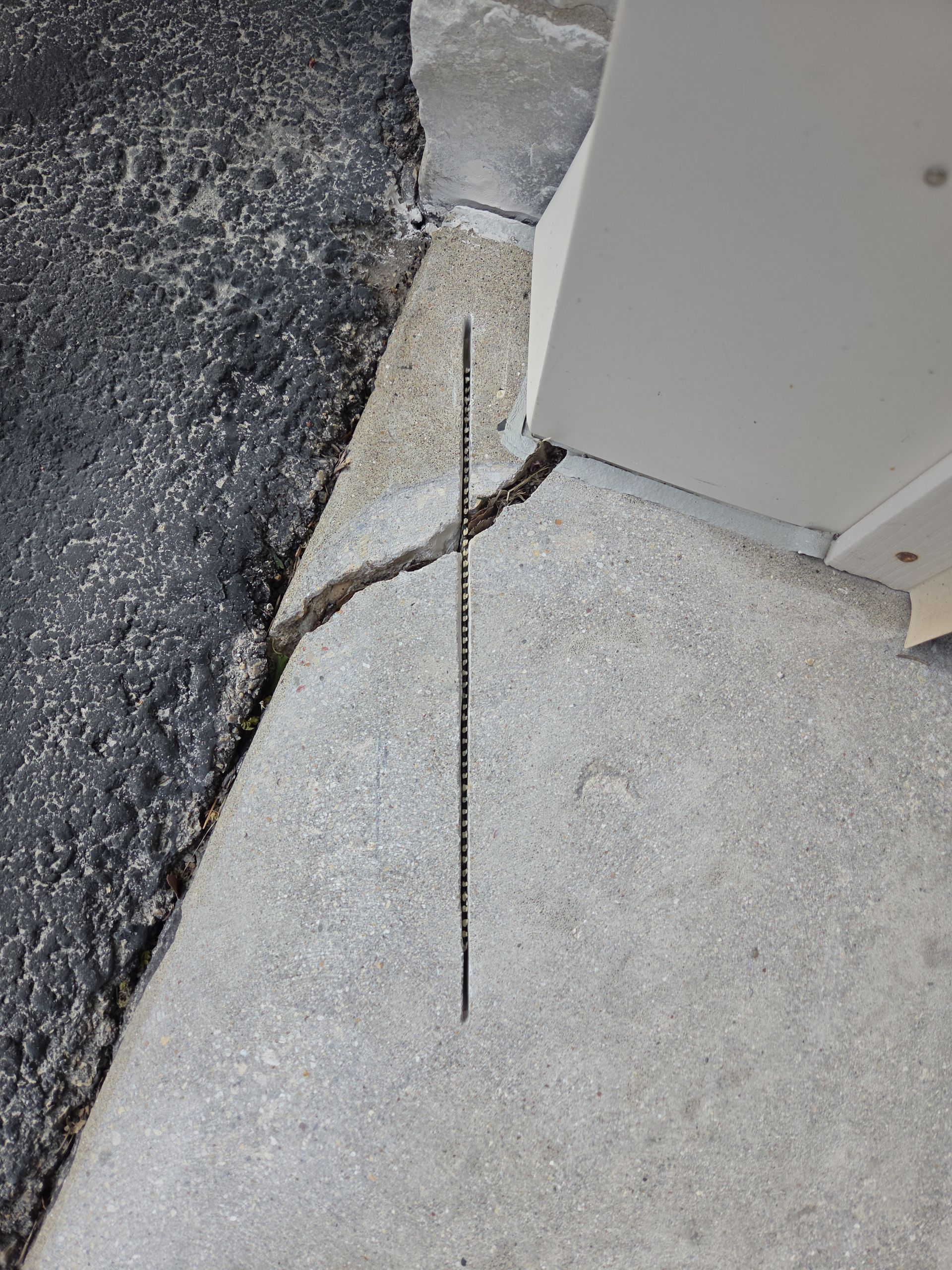 Cracked concrete walkway beside a building corner with a visible gap and uneven pavement