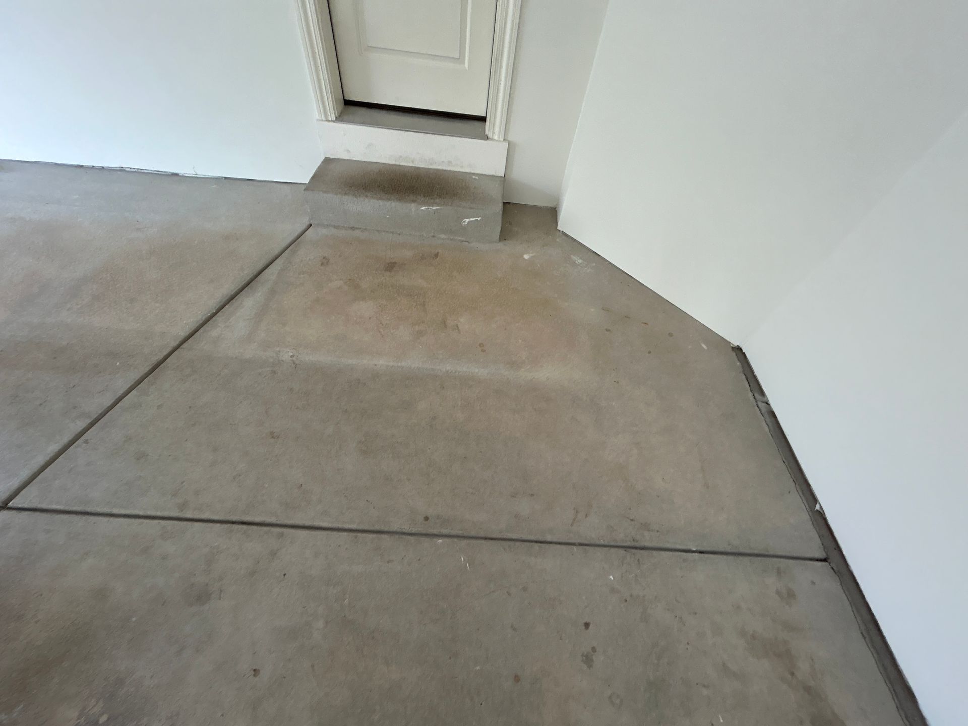 Concrete walkway leading to a white door with a small threshold step and wall corner