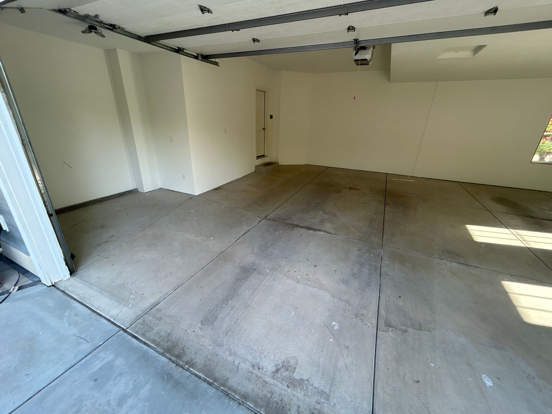 Empty garage with concrete floor, white walls, and sunlight streaming through the open door