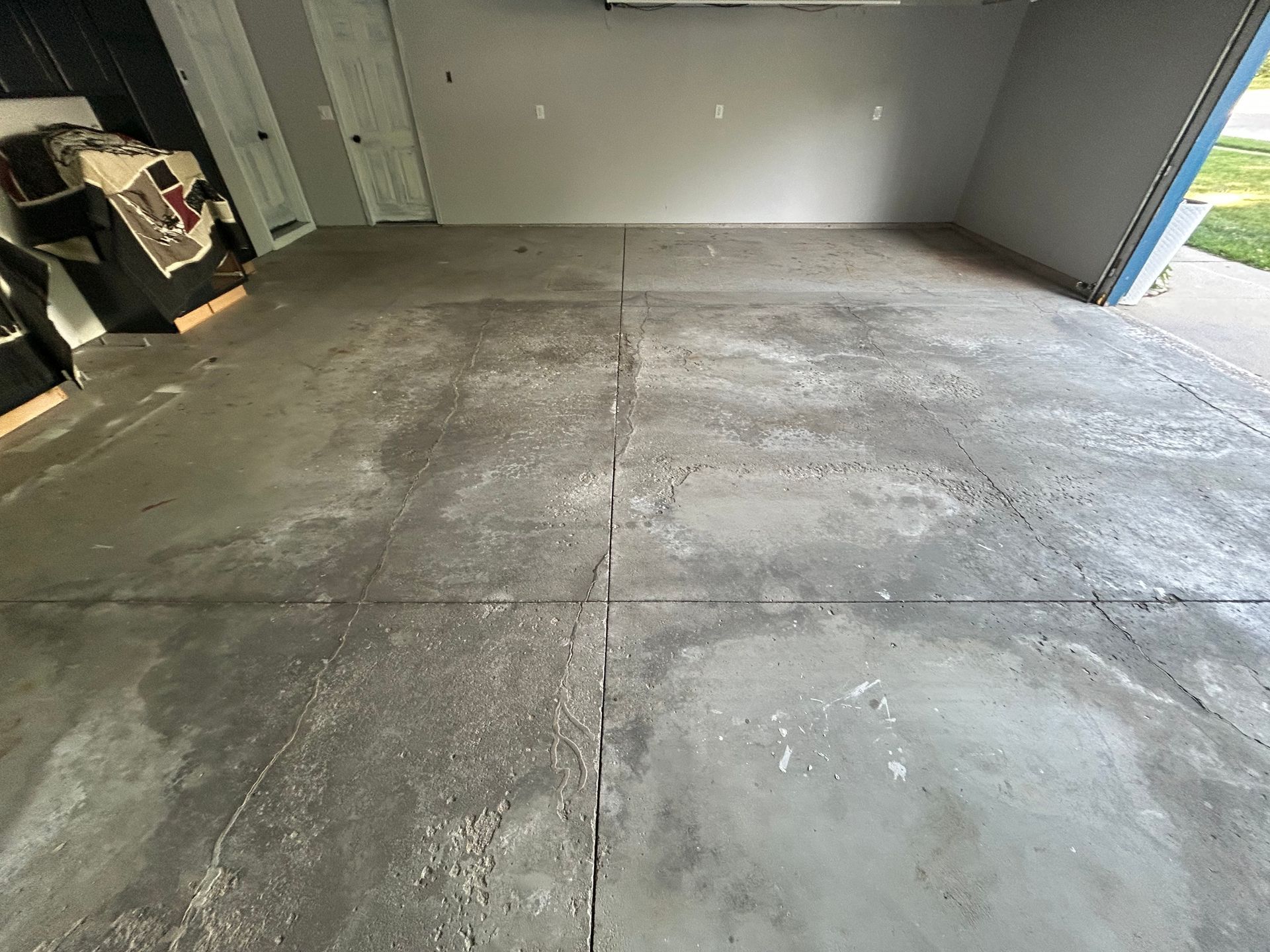 Empty concrete garage floor with visible cracks and a partially open door to the outside