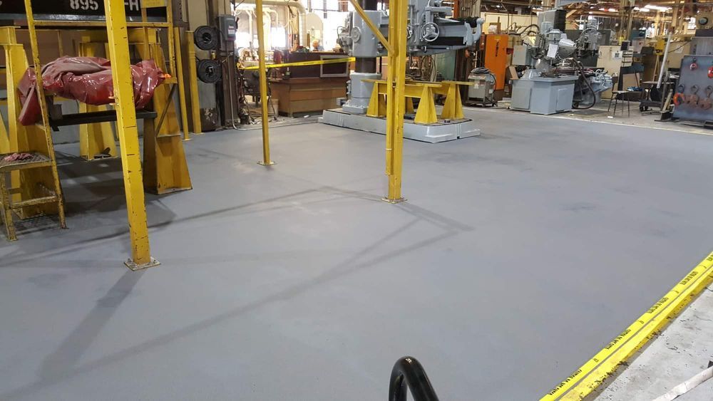 Industrial workshop floor with yellow safety posts, machinery, and a large clear gray concrete area