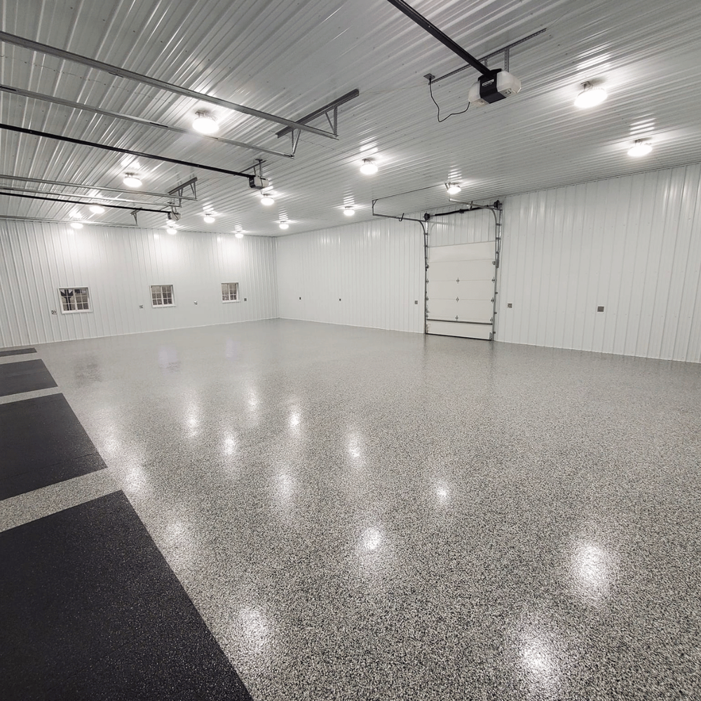 Empty white garage with speckled floor, bright ceiling lights, and a large overhead door