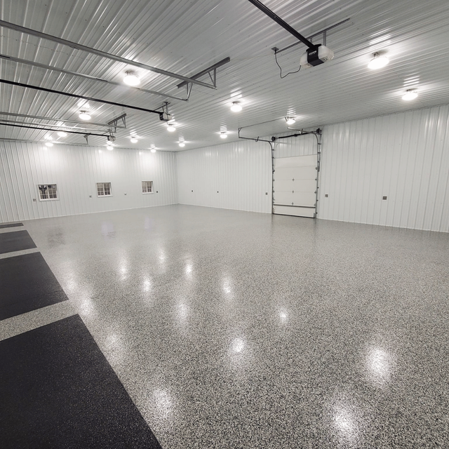 Spacious white garage or workshop with epoxy floor, overhead lights, and a large garage door