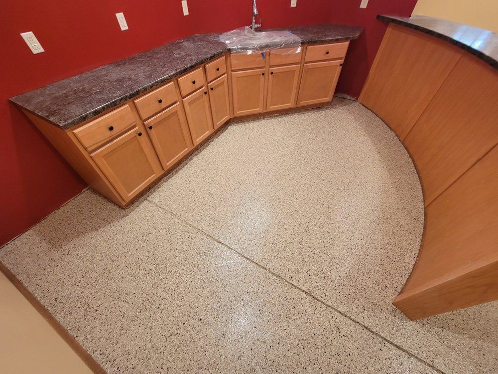 Curved kitchen counter with wood cabinets, dark granite top, and red walls on speckled tile floor