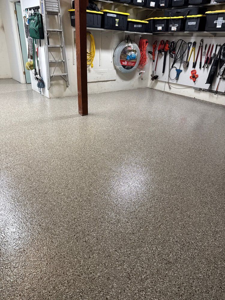 Speckled garage floor with tools hanging on a wall and a hose reel in the background