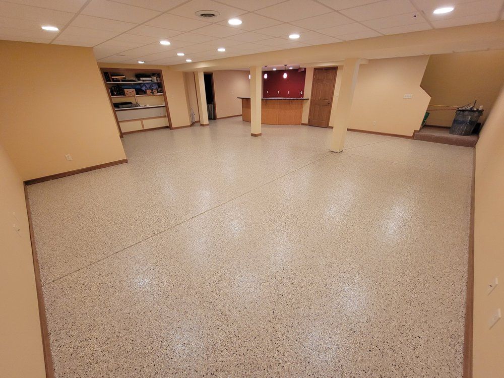 Empty beige basement room with speckled tile floor, support columns, and recessed ceiling lights