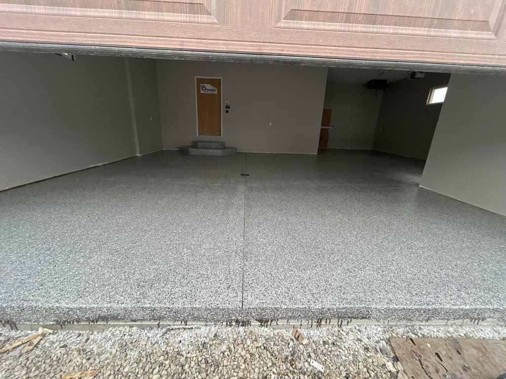 Empty open garage with a speckled gray floor and a single brown door at the back.