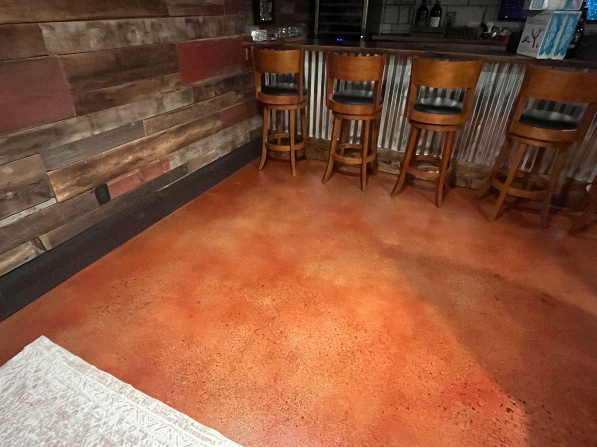 Rustic bar interior with wooden stools and an orange floor, viewed from a low angle