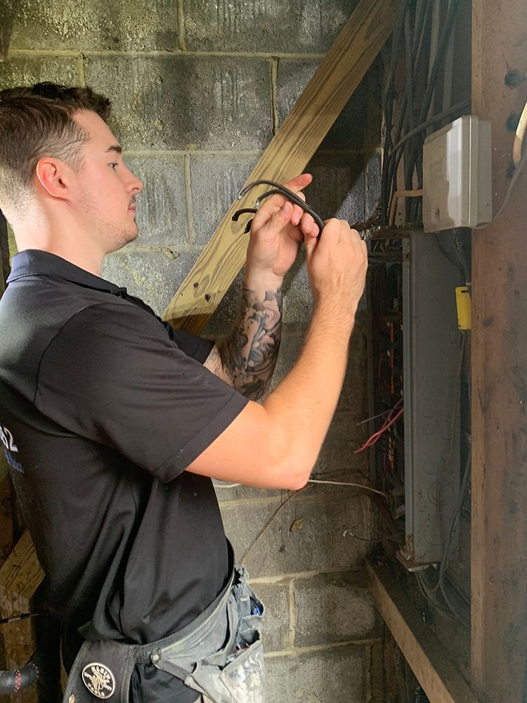 A man in black shirt wiring electrical box on a concrete wall.