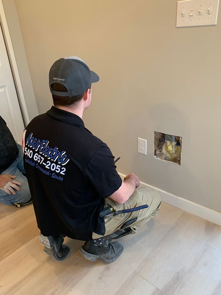 Man in uniform examines wall with hole near outlet.