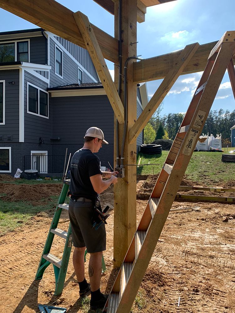 A man on a ladder works on a wooden structure outside a house.