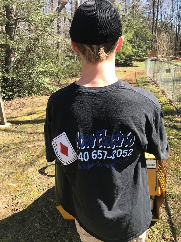Person wearing a black shirt with a diamond card logo, standing outside, with a phone number.