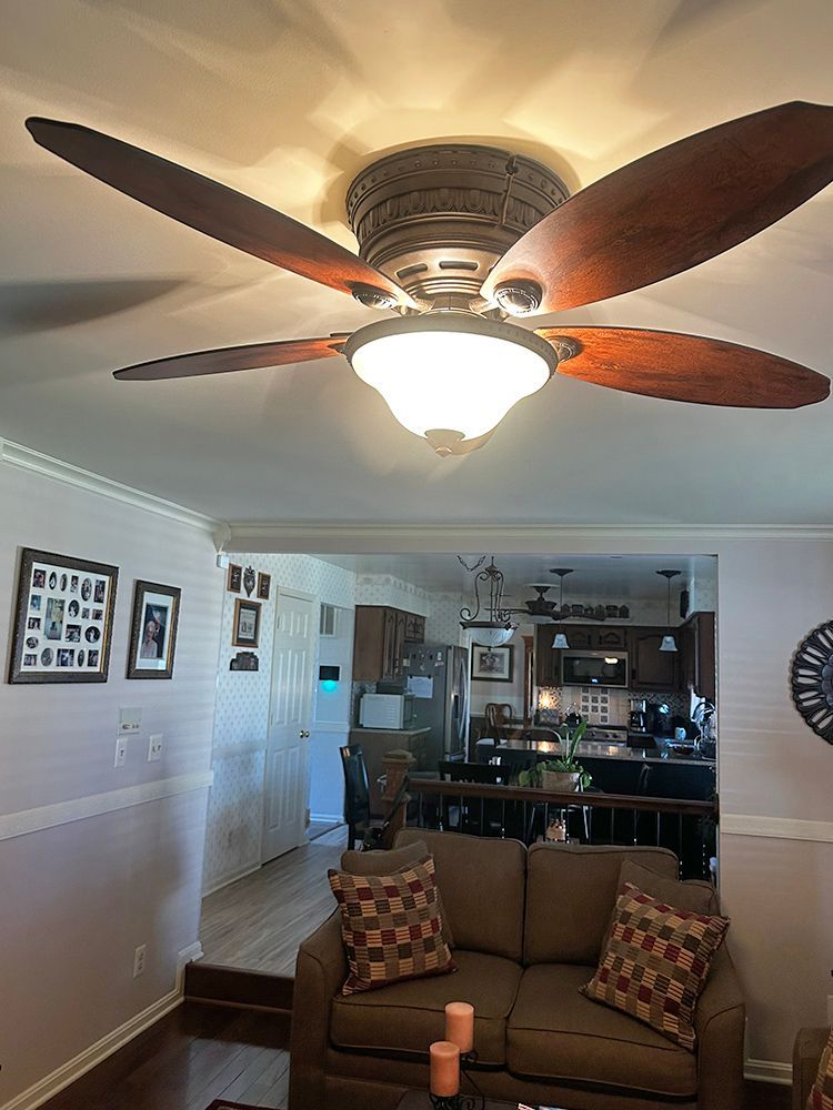 Ceiling fan with light in a living room, brown blades, above a brown couch.