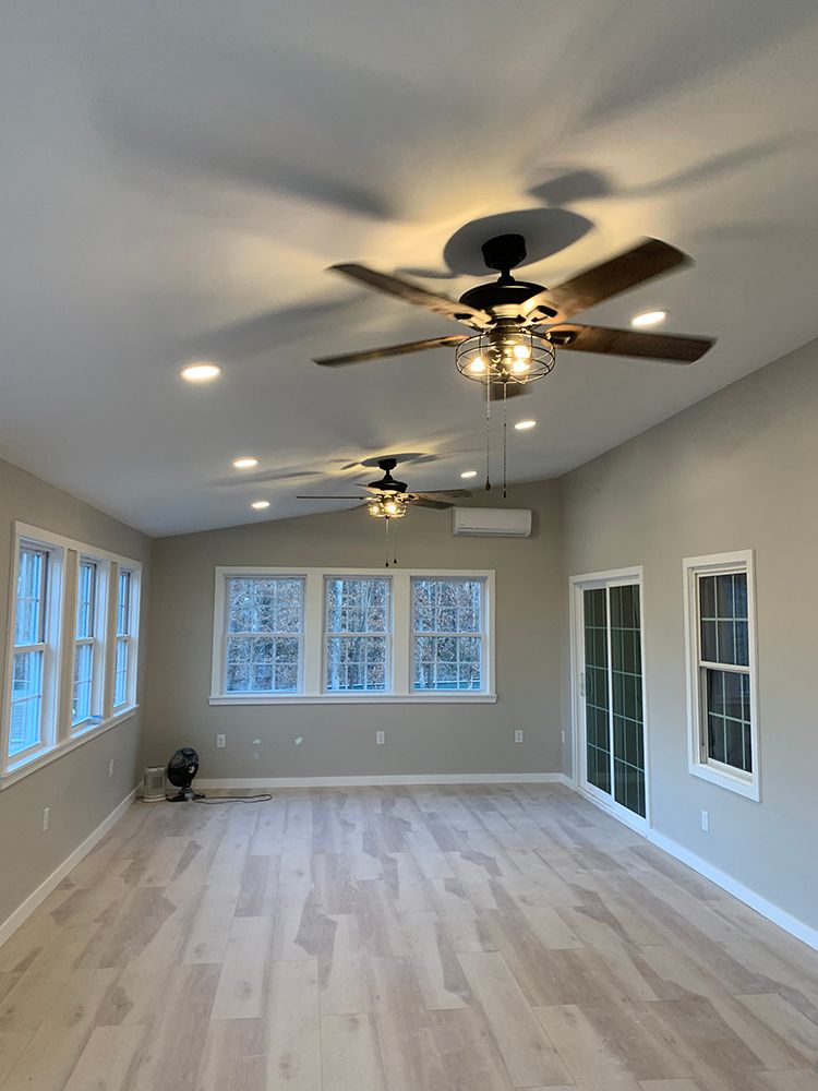 Sunroom with wooden floors, windows, ceiling fans, and recessed lighting. Light-colored walls.
