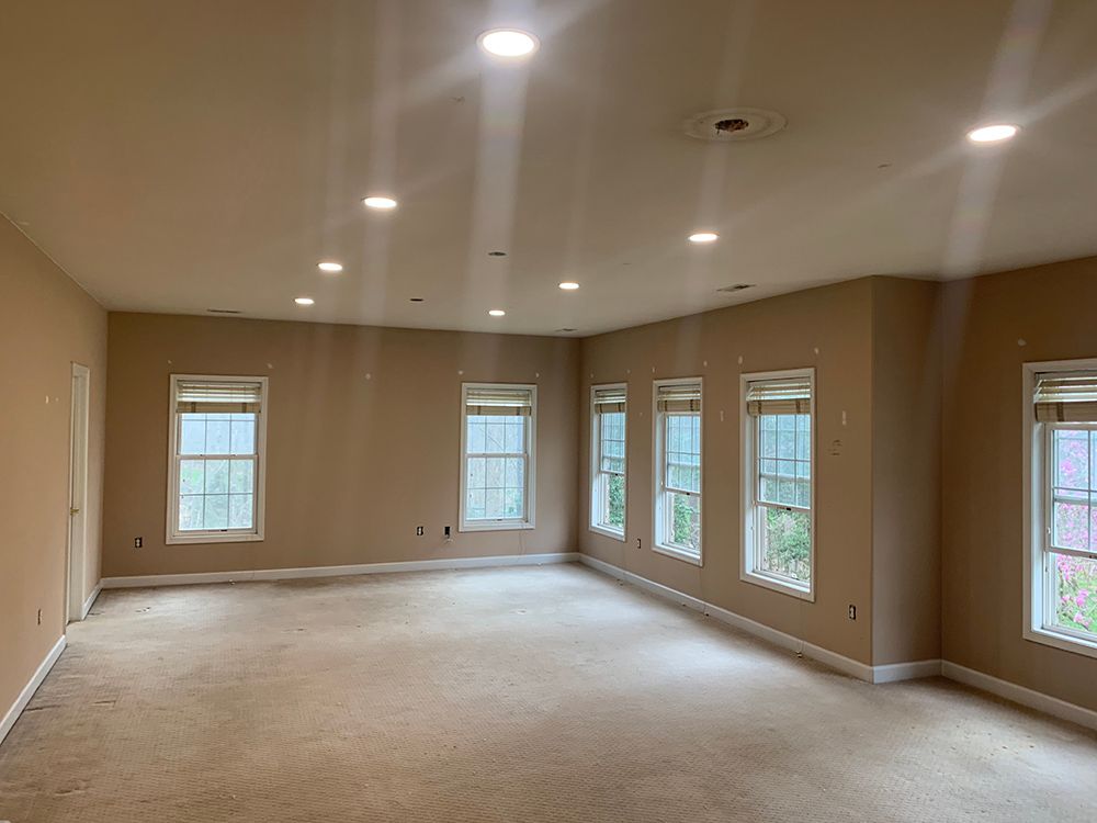 Empty beige room with windows, recessed lighting, and a worn carpet.