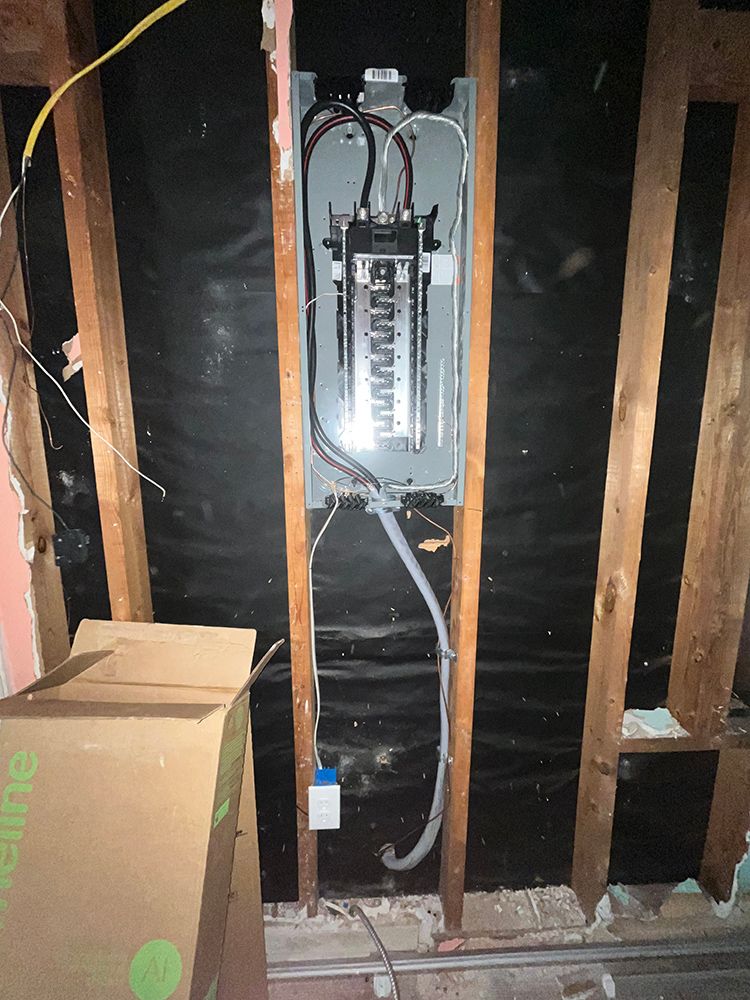 Electrical panel installed in a wall cavity, with wires and a cardboard box.