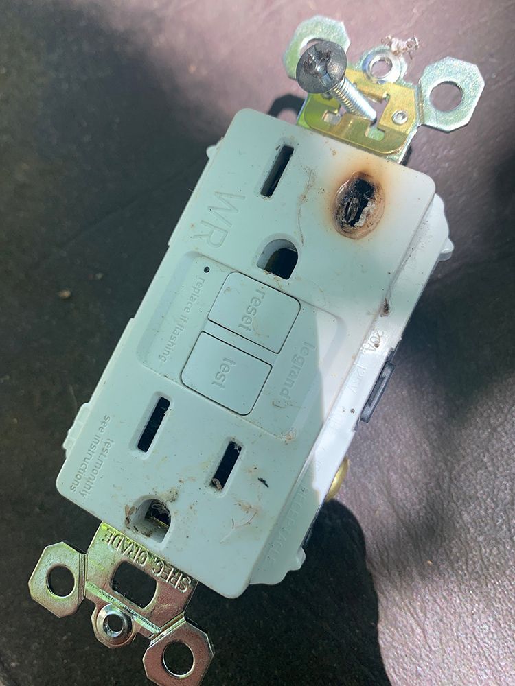 Burnt electrical outlet with a damaged faceplate.