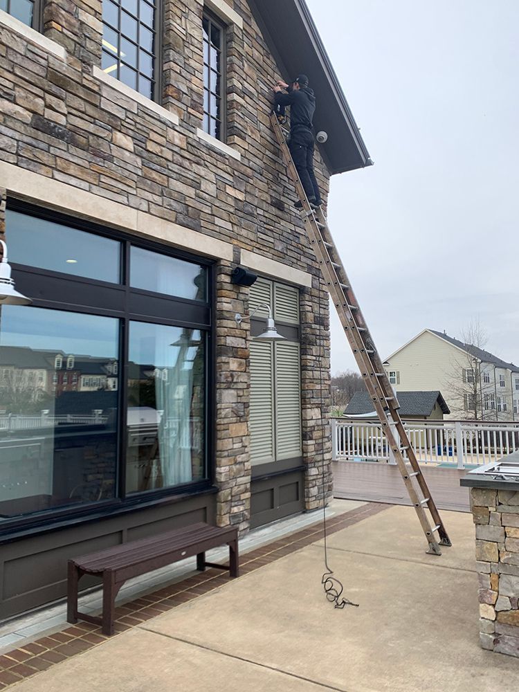 A person on a tall ladder is working on the side of a stone building, near a window and door.
