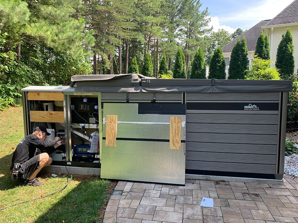 Man working on a hot tub, with panel open, on a patio outdoors.