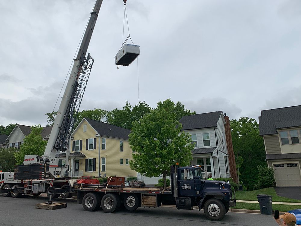 A crane lifts a large rectangular HVAC unit from a truck in a residential area.