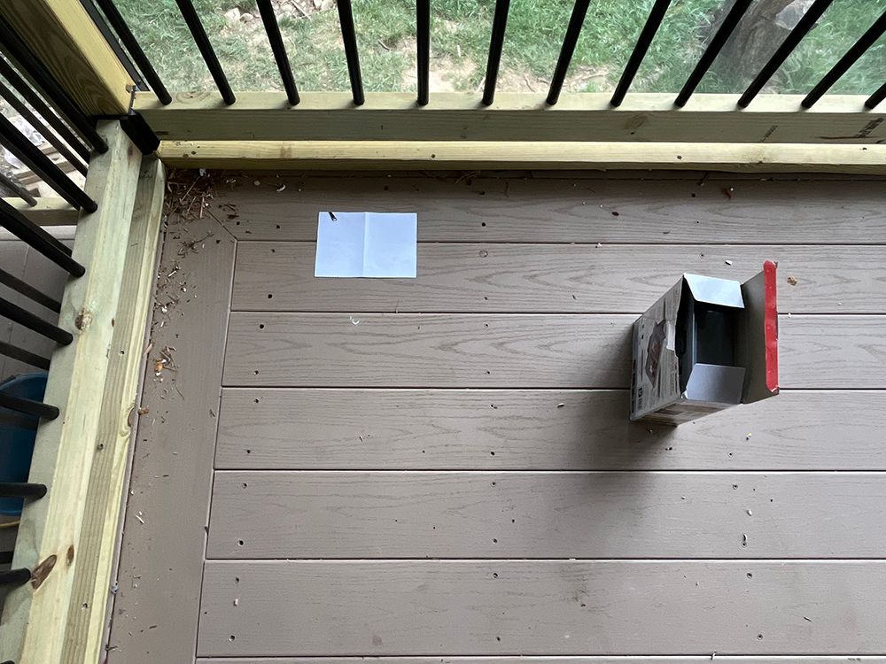 Wooden deck with a partially open cardboard box attached; sunlight.