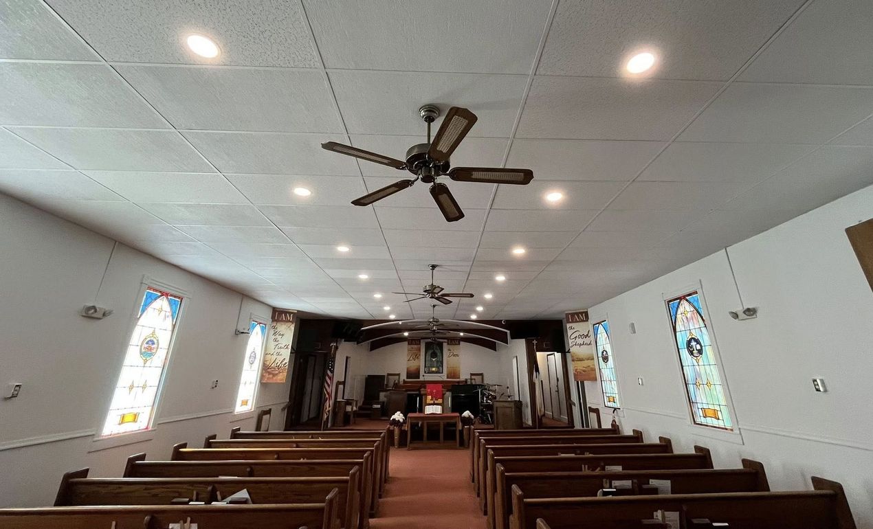 Interior of a church with rows of wooden pews, stained glass windows, and a ceiling fan.