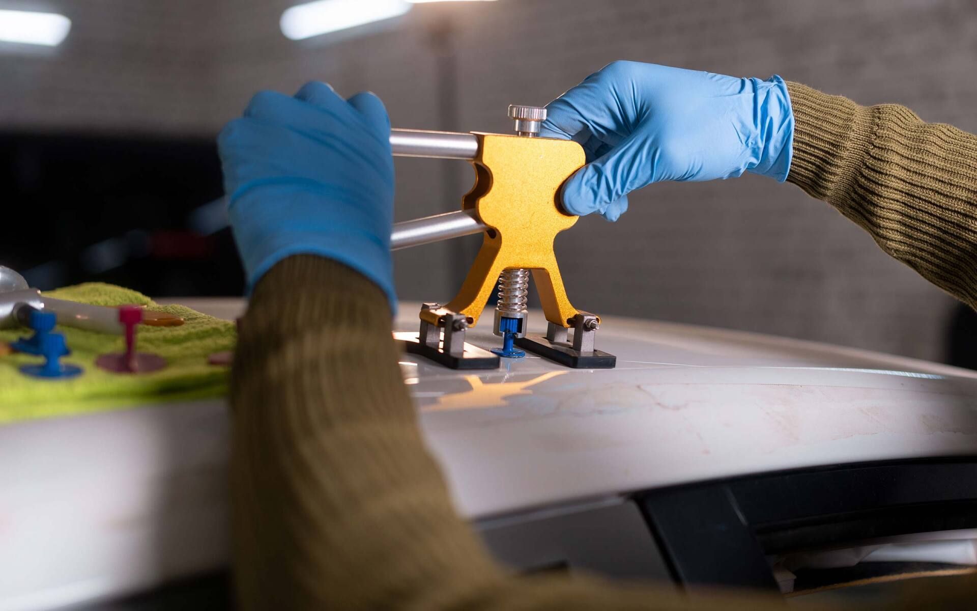 Gloved hands placing a small yellow 3D-printed part on a workbench with tools nearby