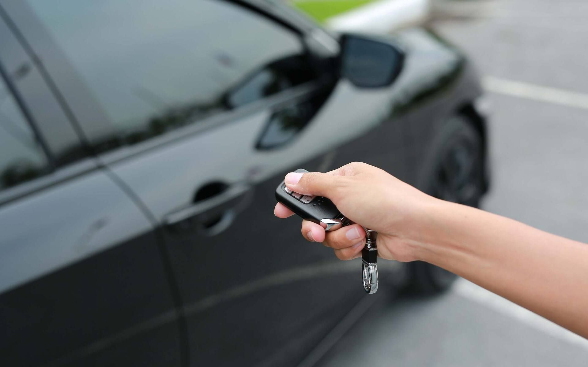 Hand holding car key fob near a black car door to unlock it
