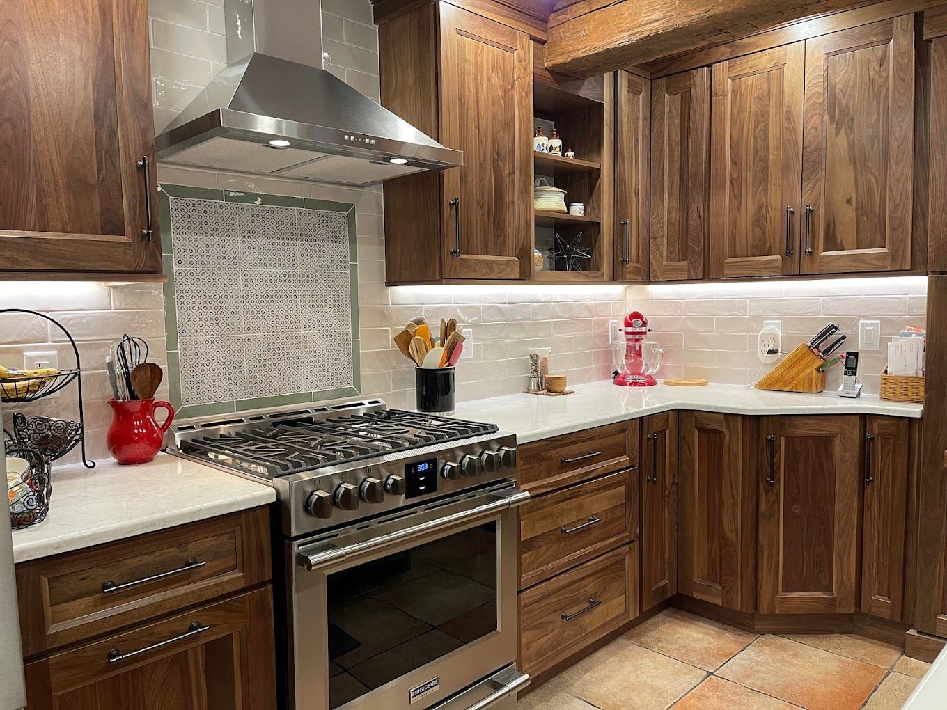 Wooden kitchen with stainless steel stove, range hood, white countertops, and mosaic backsplash.