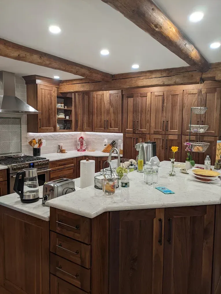 Rustic kitchen with wooden cabinets, white countertops, exposed beams, and a large island set with dishes and glasses