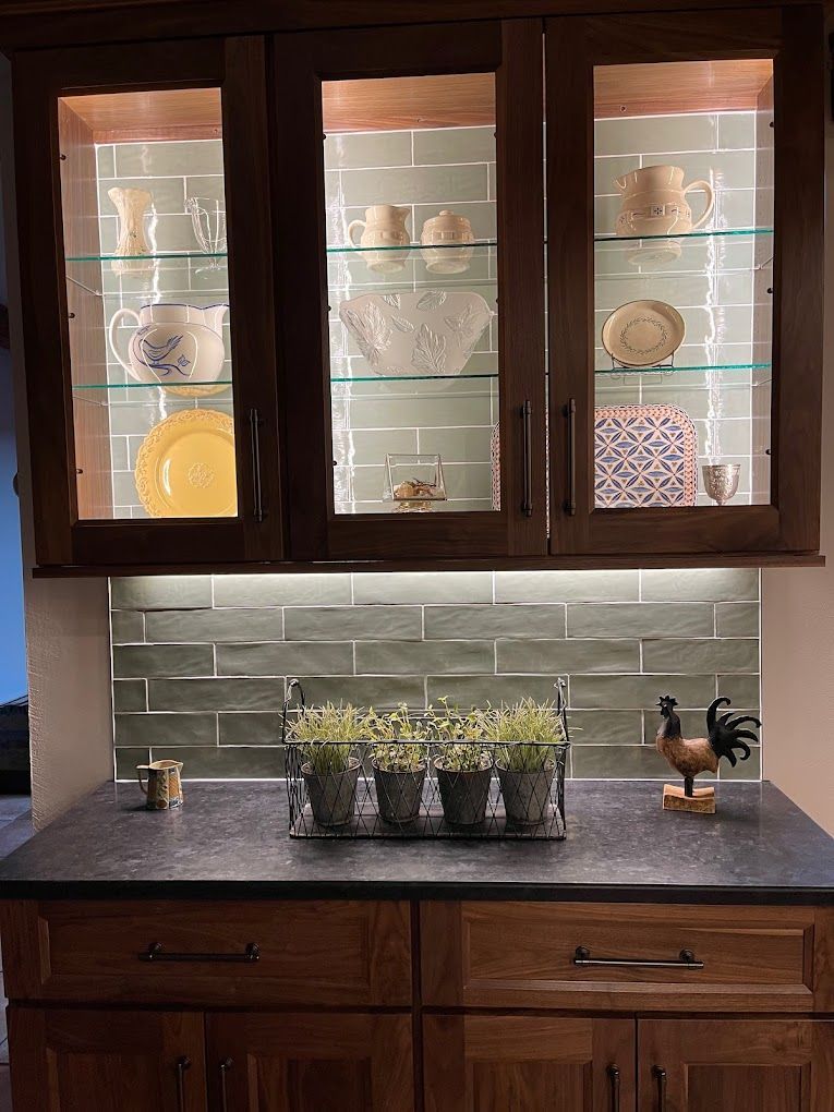 Kitchen cabinets with frosted glass, a gray tile backsplash, and potted herbs on the counter