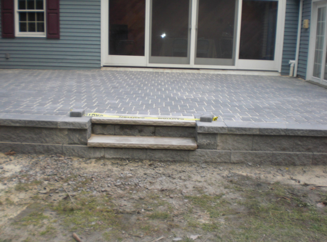 Stone patio with steps leading to a lower level, against a blue house with sliding doors.
